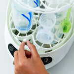 Eine Hand legt einen kleinen weißen Gegenstand in den Babybrezza.de Bottle Washer Pro: Babyflaschenreiniger zum Waschen, Sterilisieren und Trocknen, gefüllt mit Flaschen und Teilen, mit Bedienknöpfen und fortschrittlicher HEPA-Trocknung auf der Vorderseite. - product thumbnail